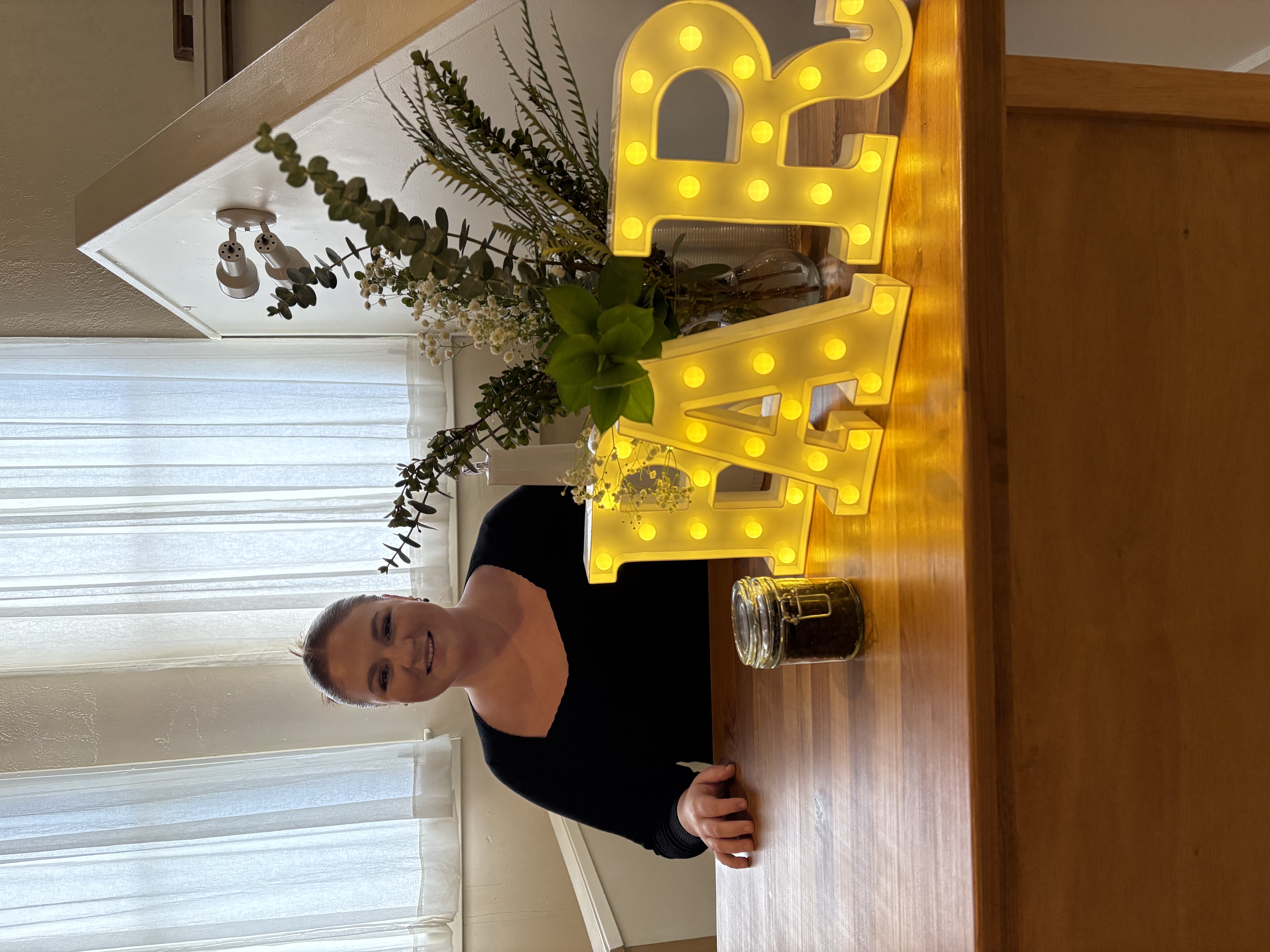 Sarah working behind a bar at an indoor event with a lit 'bar' sign and flower decorations