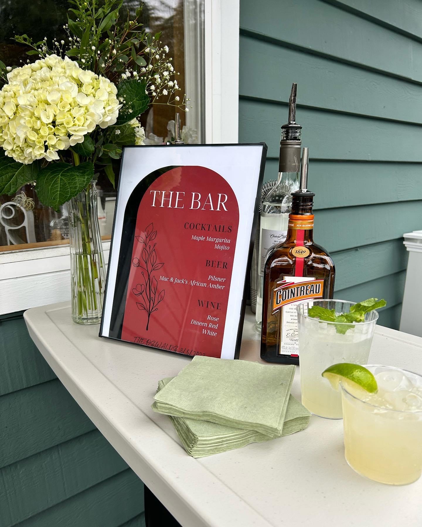 a mojito and margarita with a Cointreau bottle and cocktail menu on an outdoor bar with white tablecloth